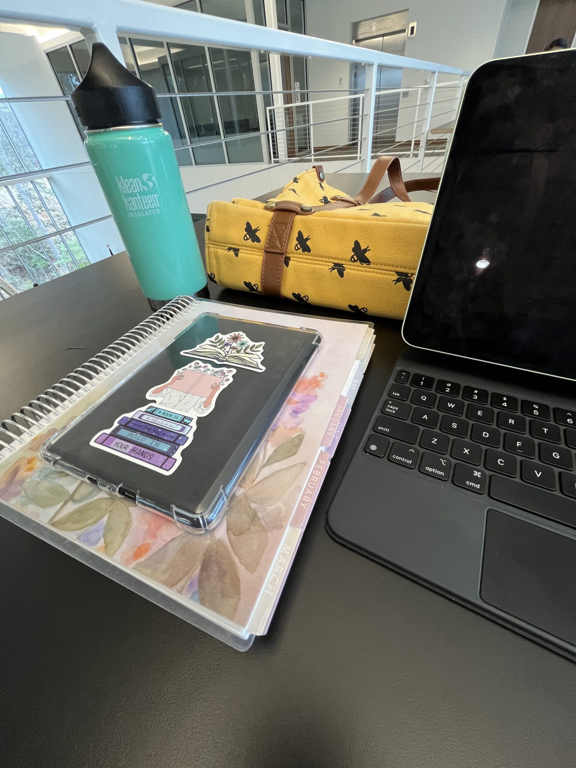 Picture of Lindsey's writing necessities, including laptop, planner, Kindle, water bottle, and purse.